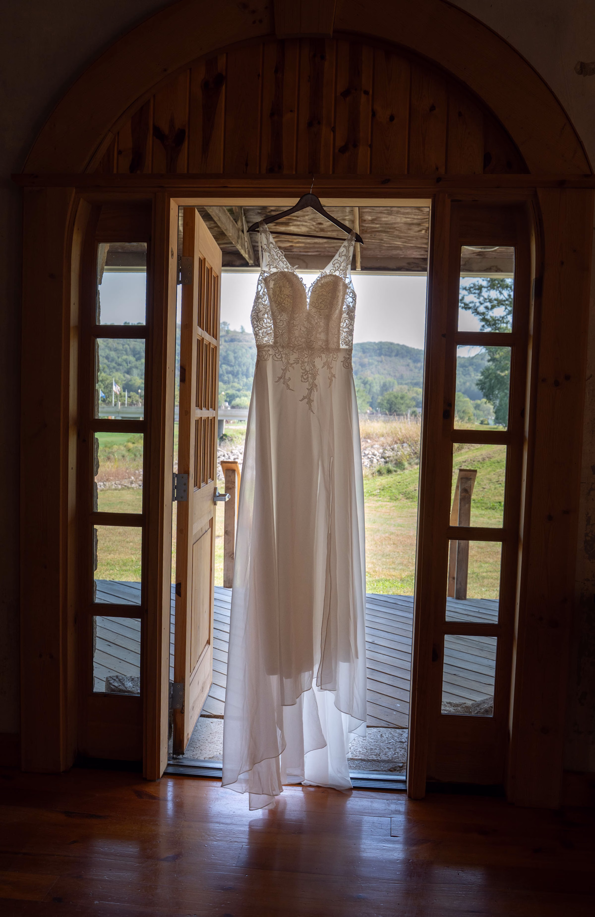 Lace wedding dress hanging in an arched wooden doorway overlooking the countryside at The Mill on Rush Creek in Rushford, MN