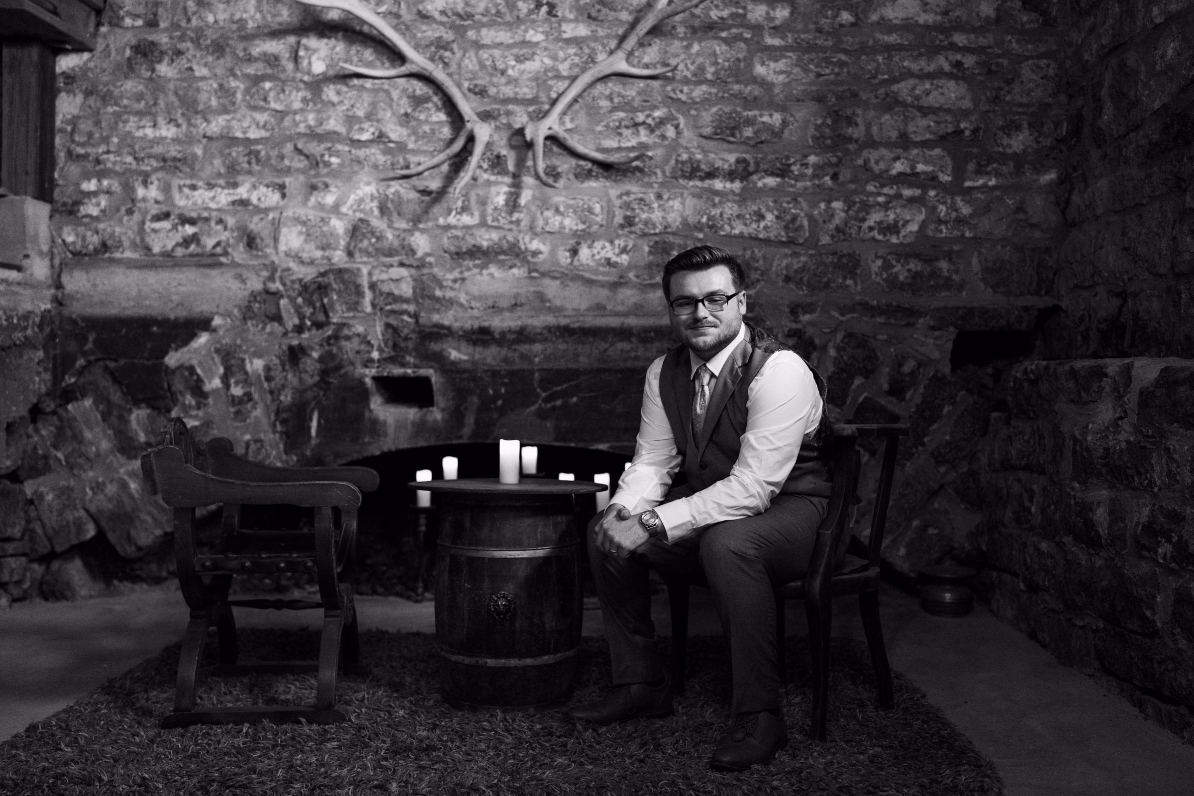 Groom seated by the stone fireplace at The Mill on Rush Creek wedding venue in Rushford, Minnesota