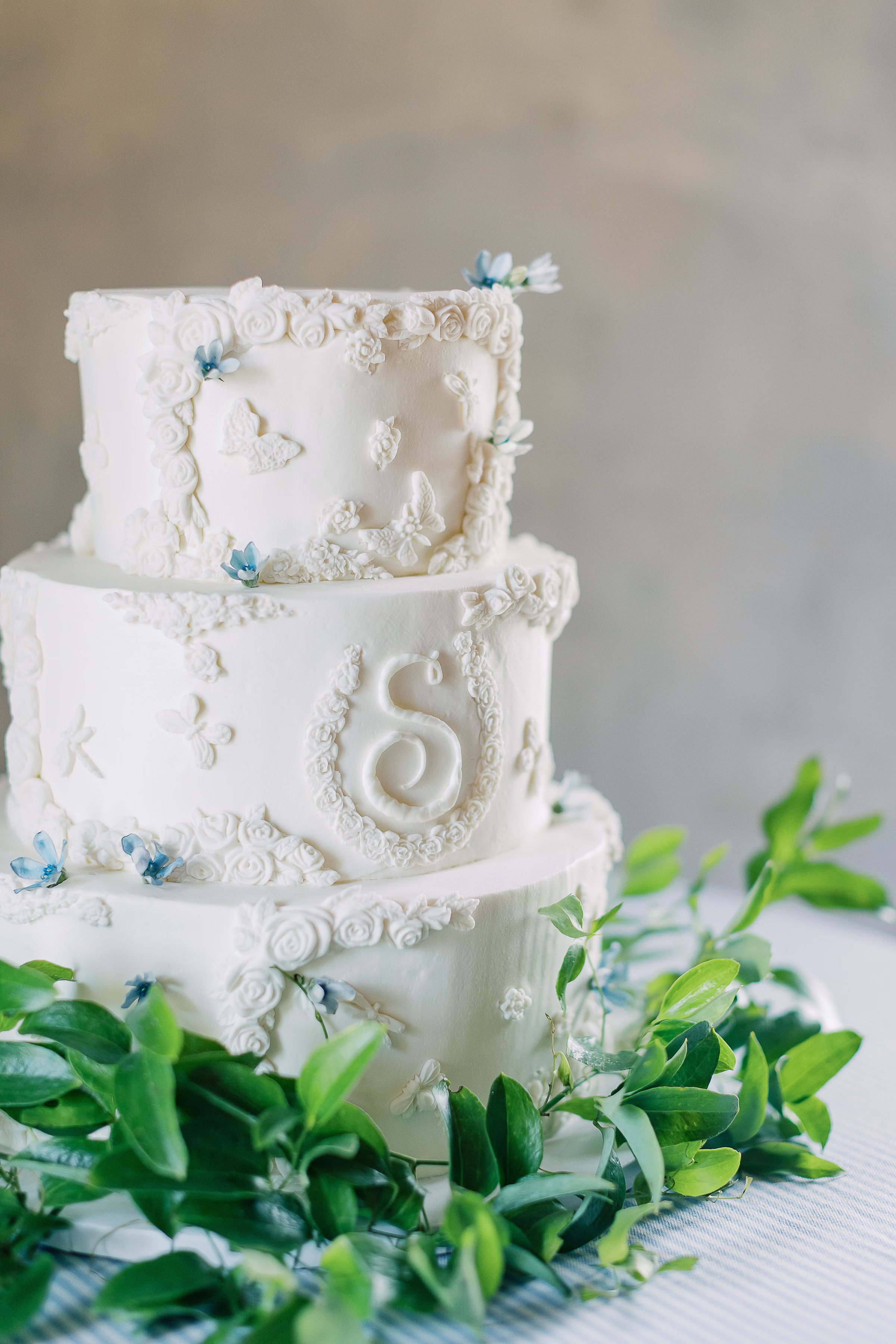 Three-tier white wedding cake decorated with intricate piped details and blue flowers