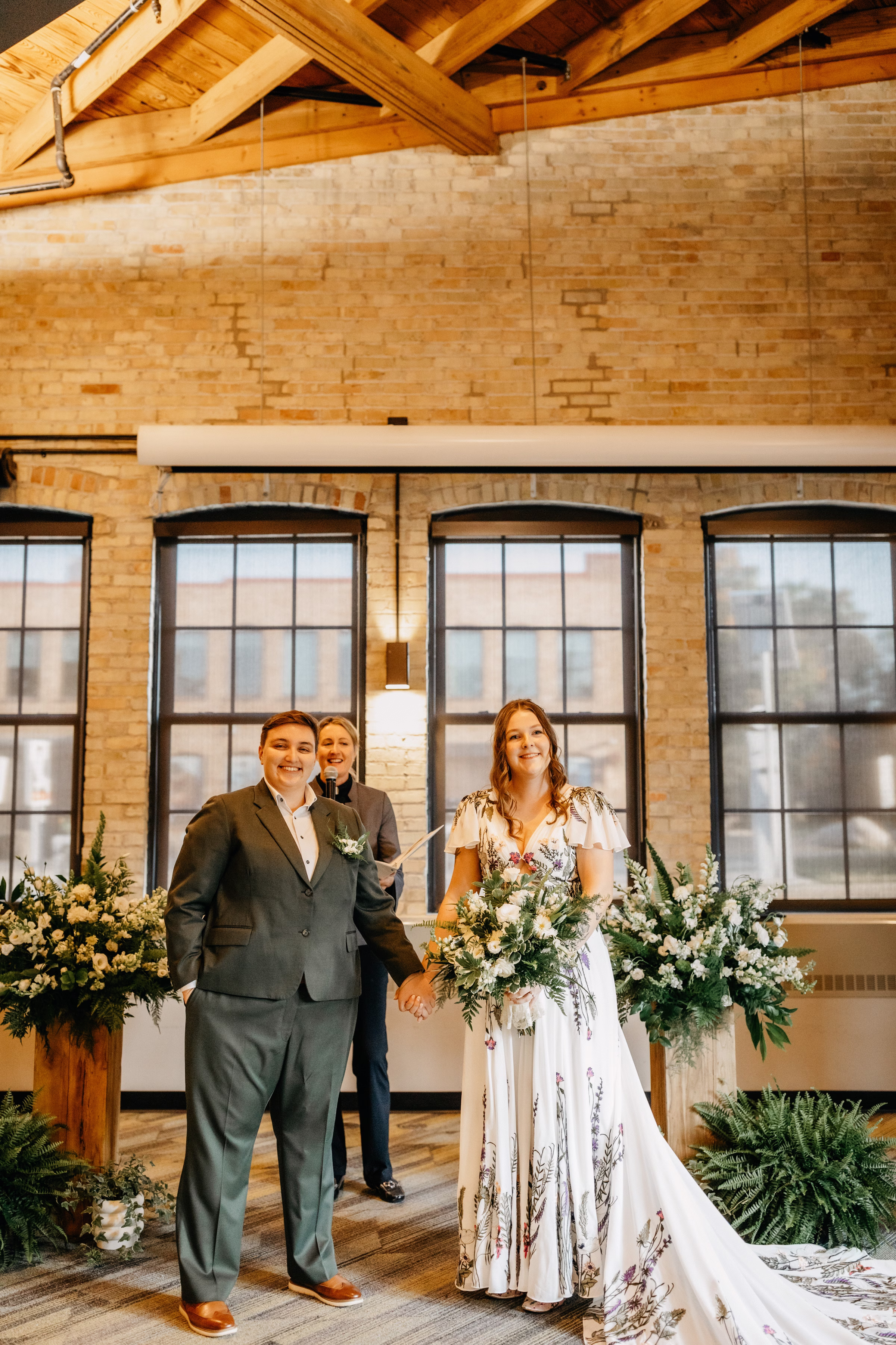 Sam and Janine hold hands at their ceremony, smiling out at their attendees
