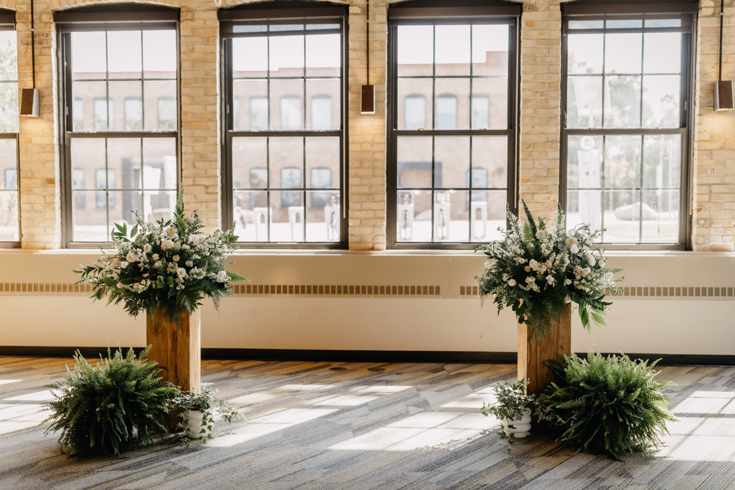 a front view of the ceremony backdrop, including florals placed on two wooden pedestals, and greenery arrangements on the floor beside them