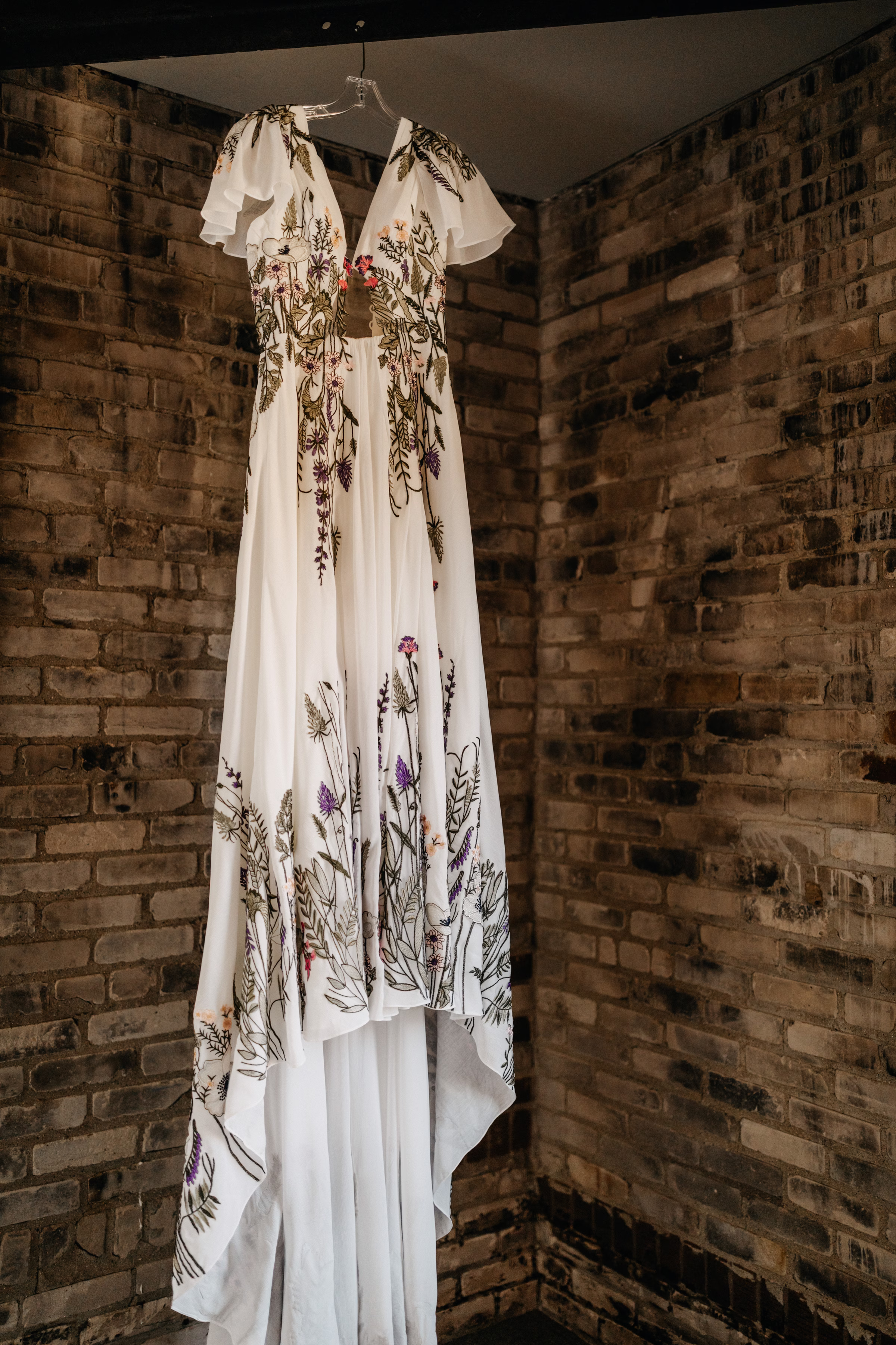 a detail photo of a wedding dress on a hanger, showing the detailed and colorful embroidery elements on the fabric
