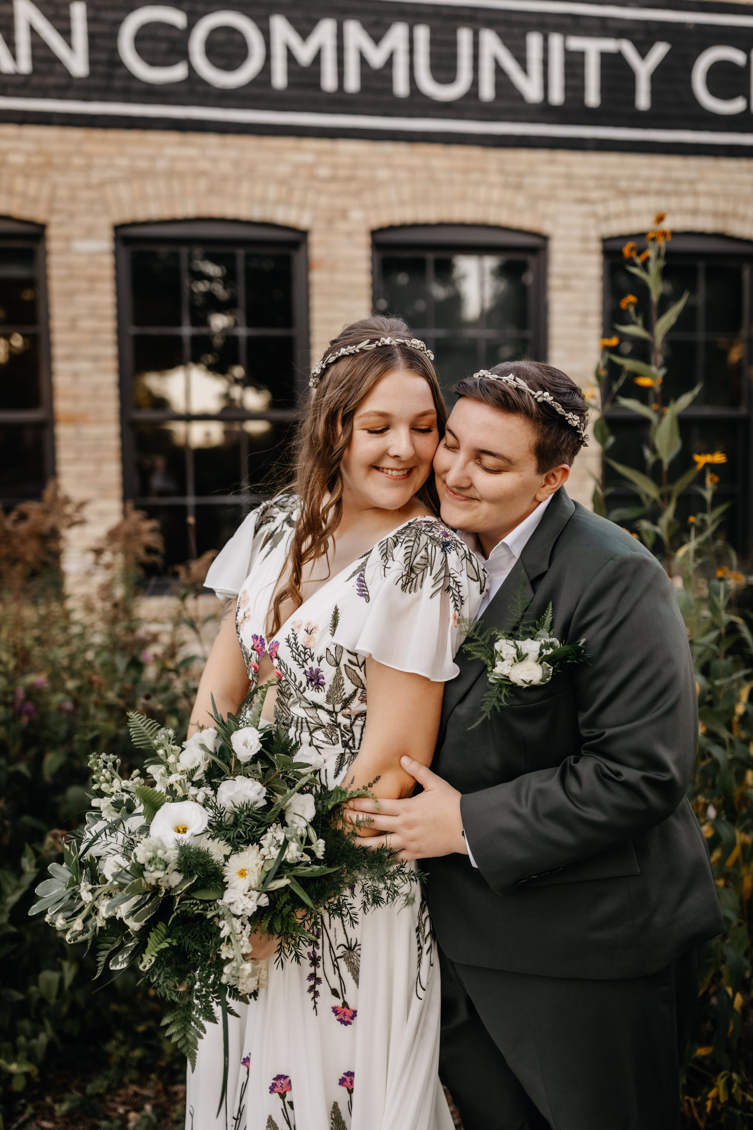 Sam & Janine embrace in front of Goodman Community Center. Sam holds her bouquet from Melody Rose Designs that matches Janine's boutonniere