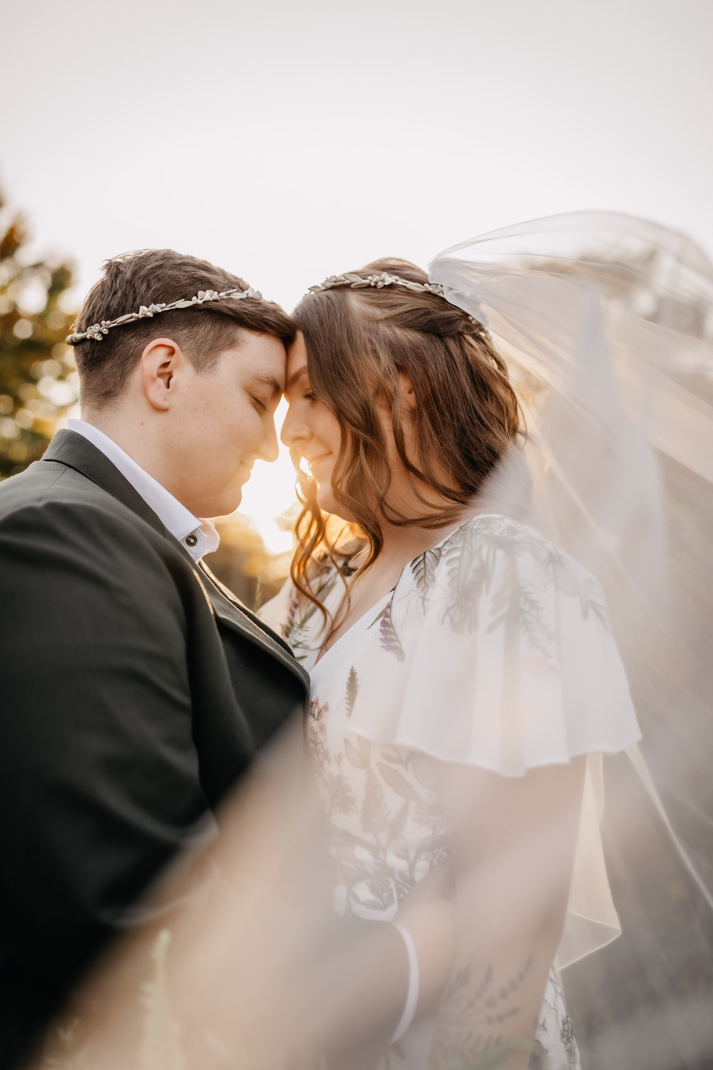 a sunset photo of the brides facing each other as Sam's veil floats in the wind