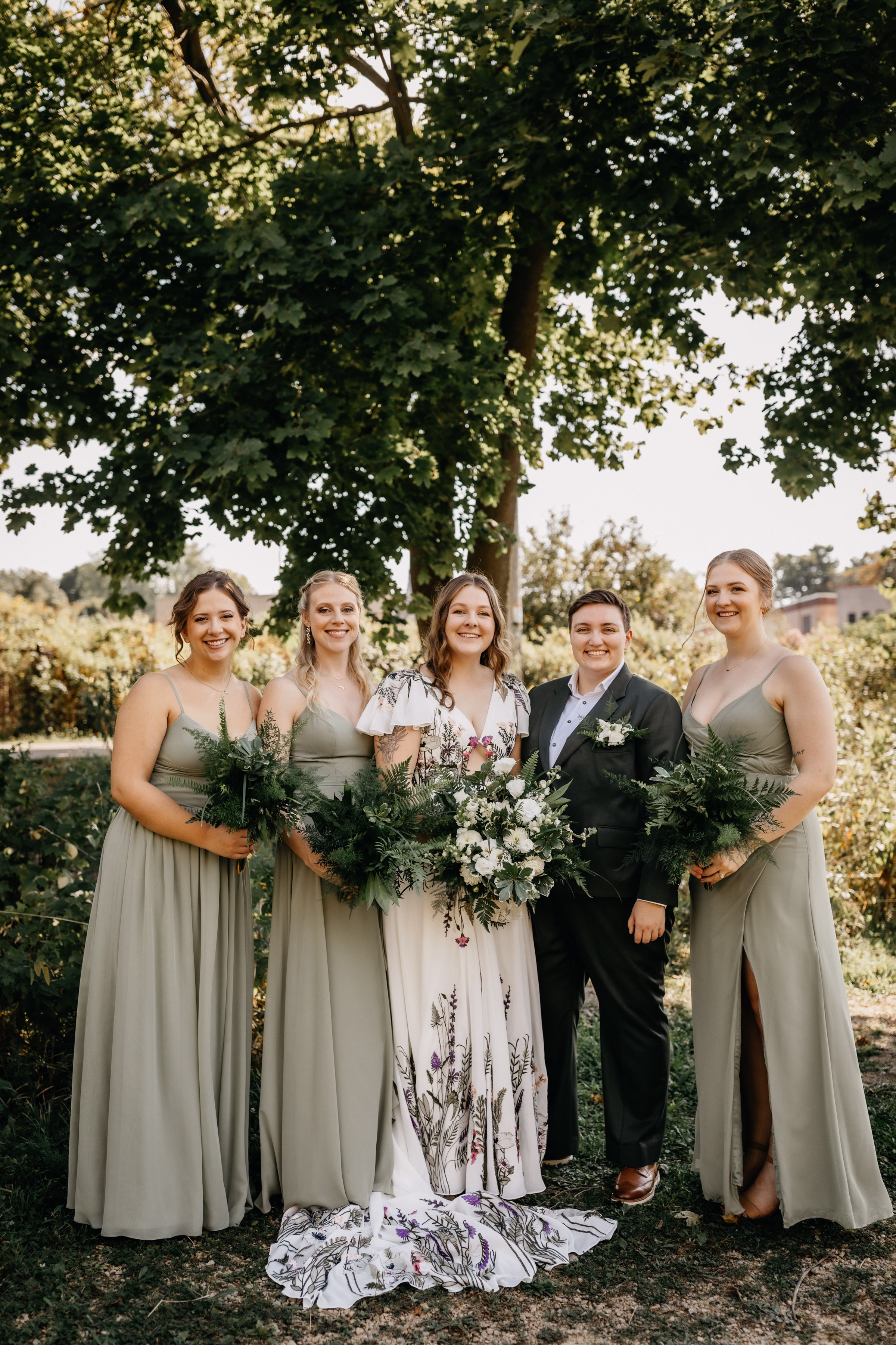 the couple poses beside their bridesmaids dressed in sage green