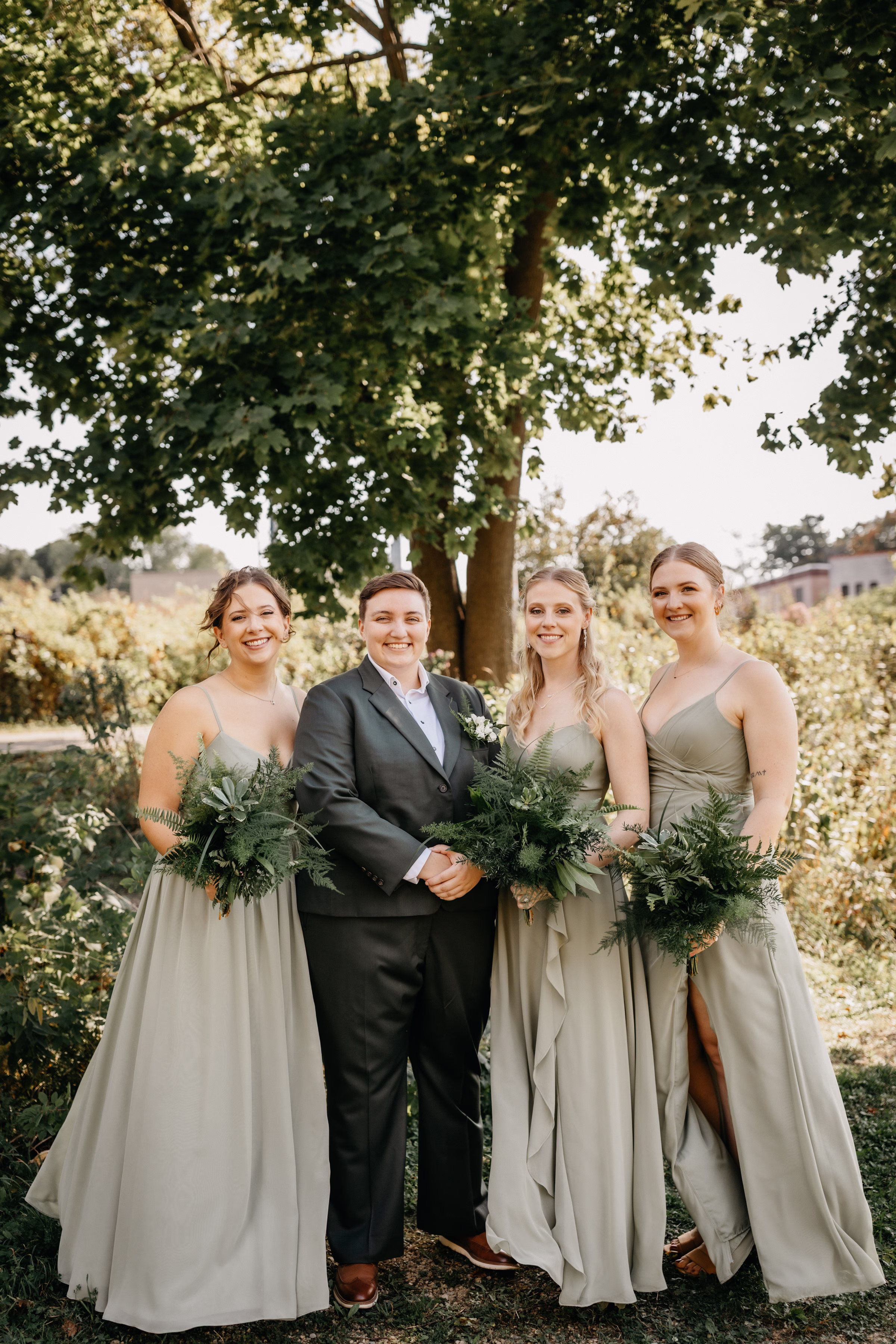 Janine smiles alongside her wedding party dressed in sage green dresses