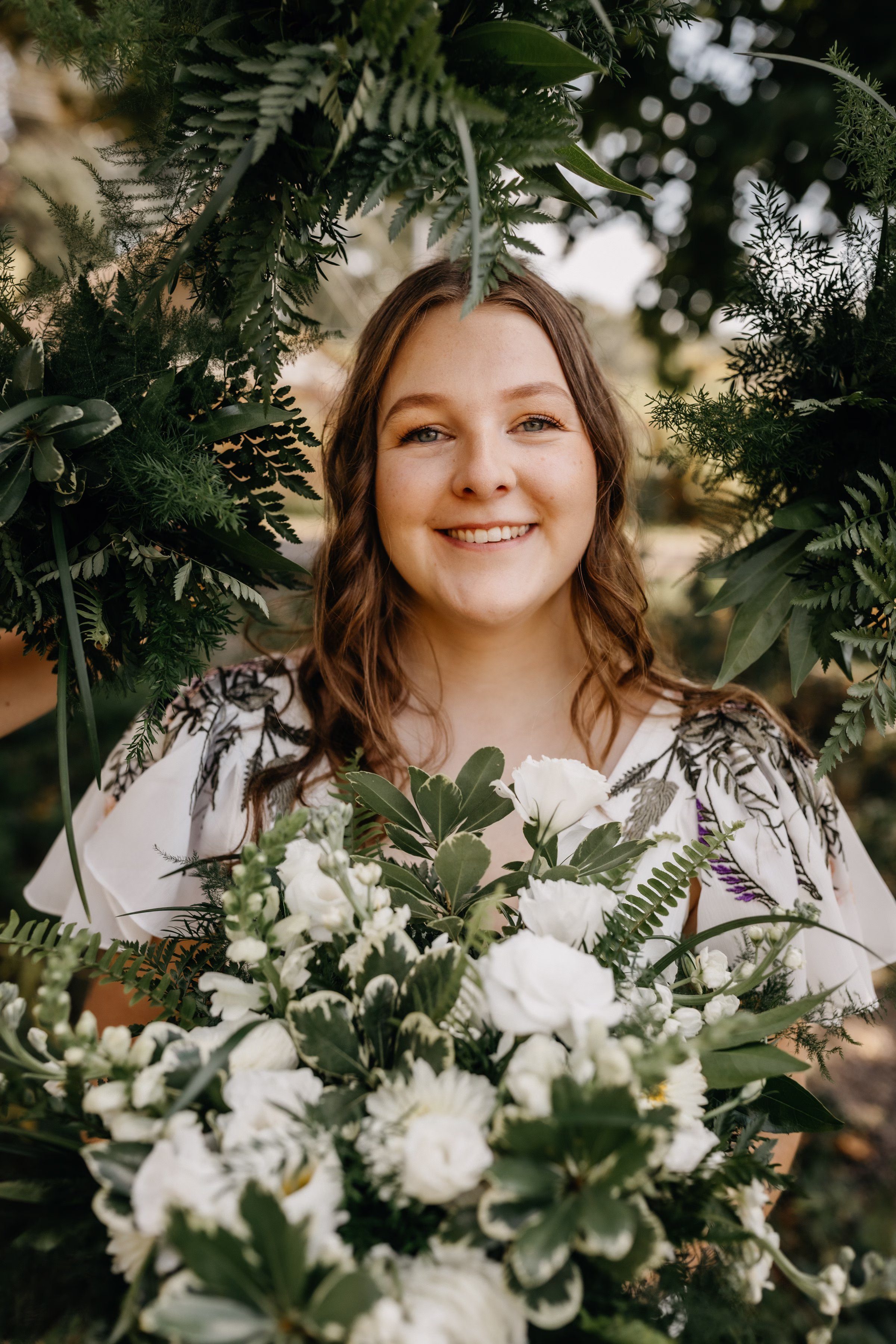 a close up of Sam smiling while her wedding party holds their bouquets around her, framing her in florals and greenery