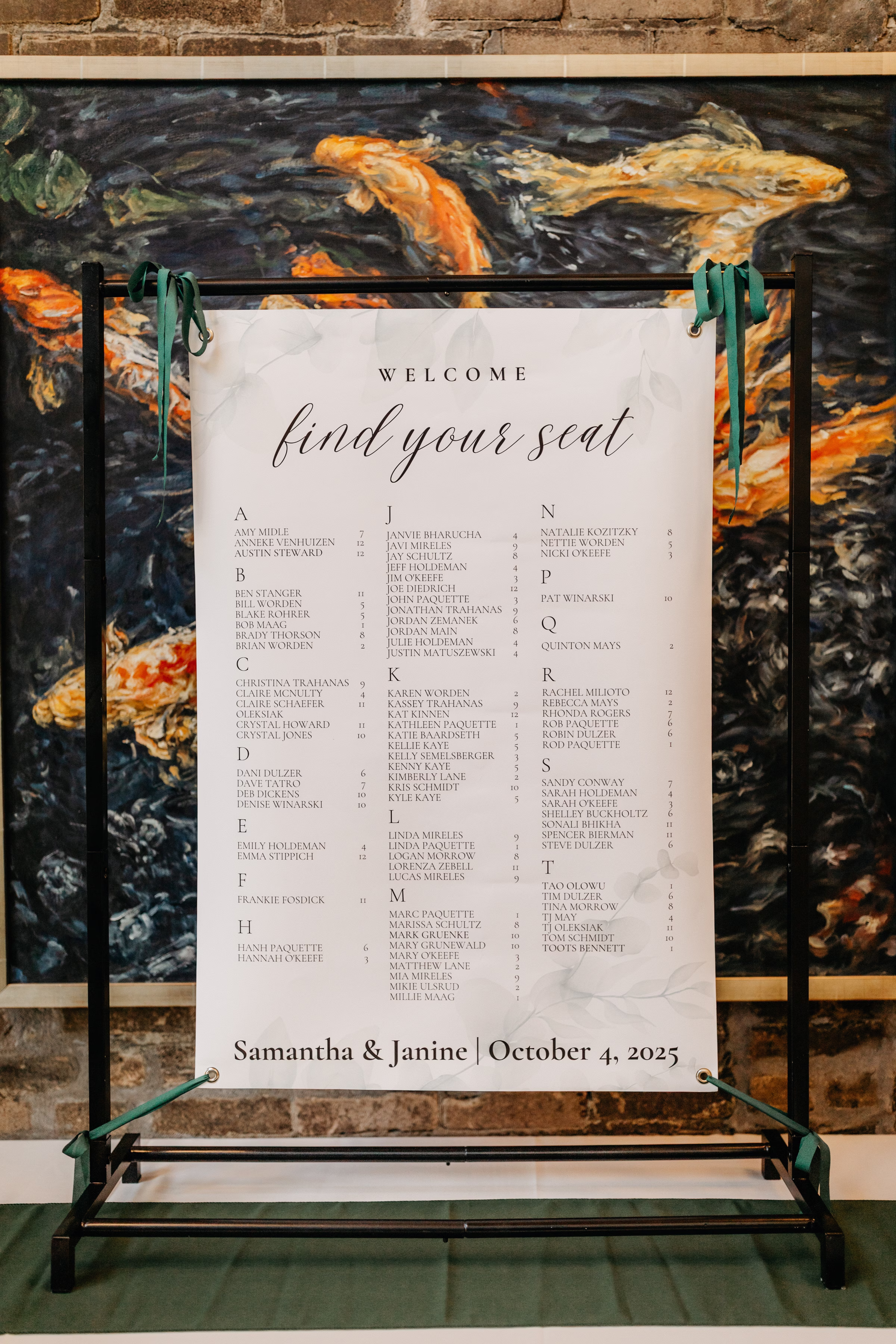 a seating chart sign attached to a black sign holder with green ribbons