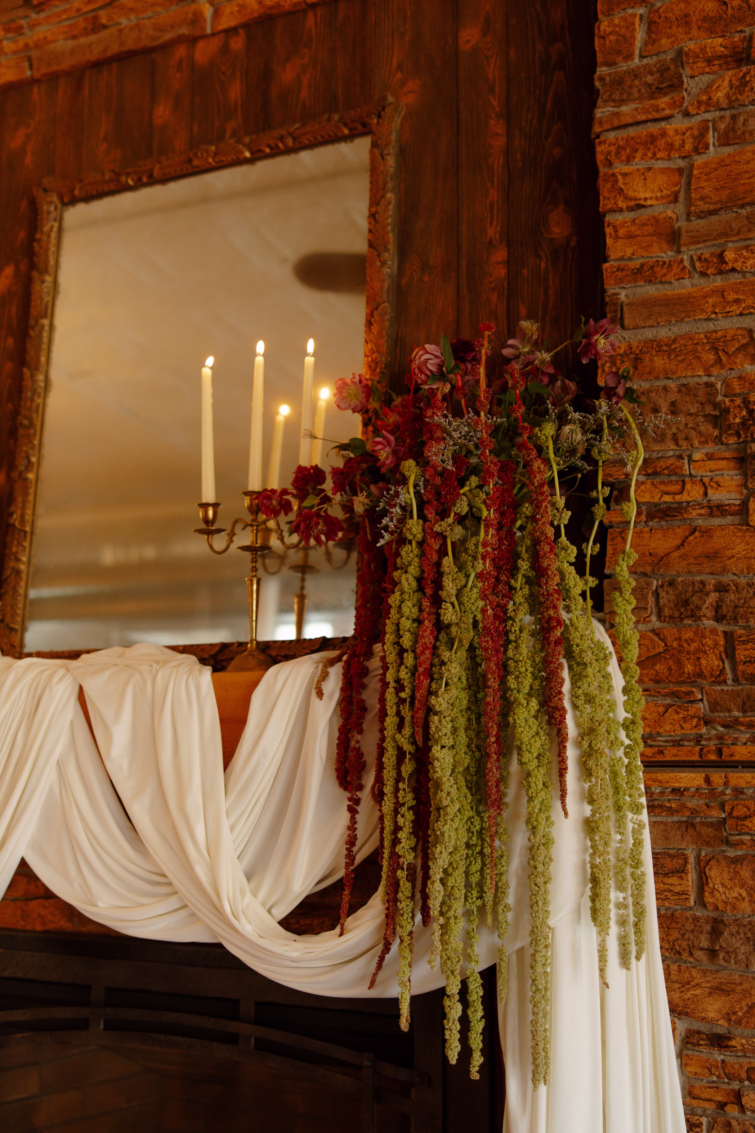 a detail photo of the draping and florals along the fireplace in the lounge at B's Place Event Venue in La Crosse, Wisconsin. Florals consist of red and green amaranthus