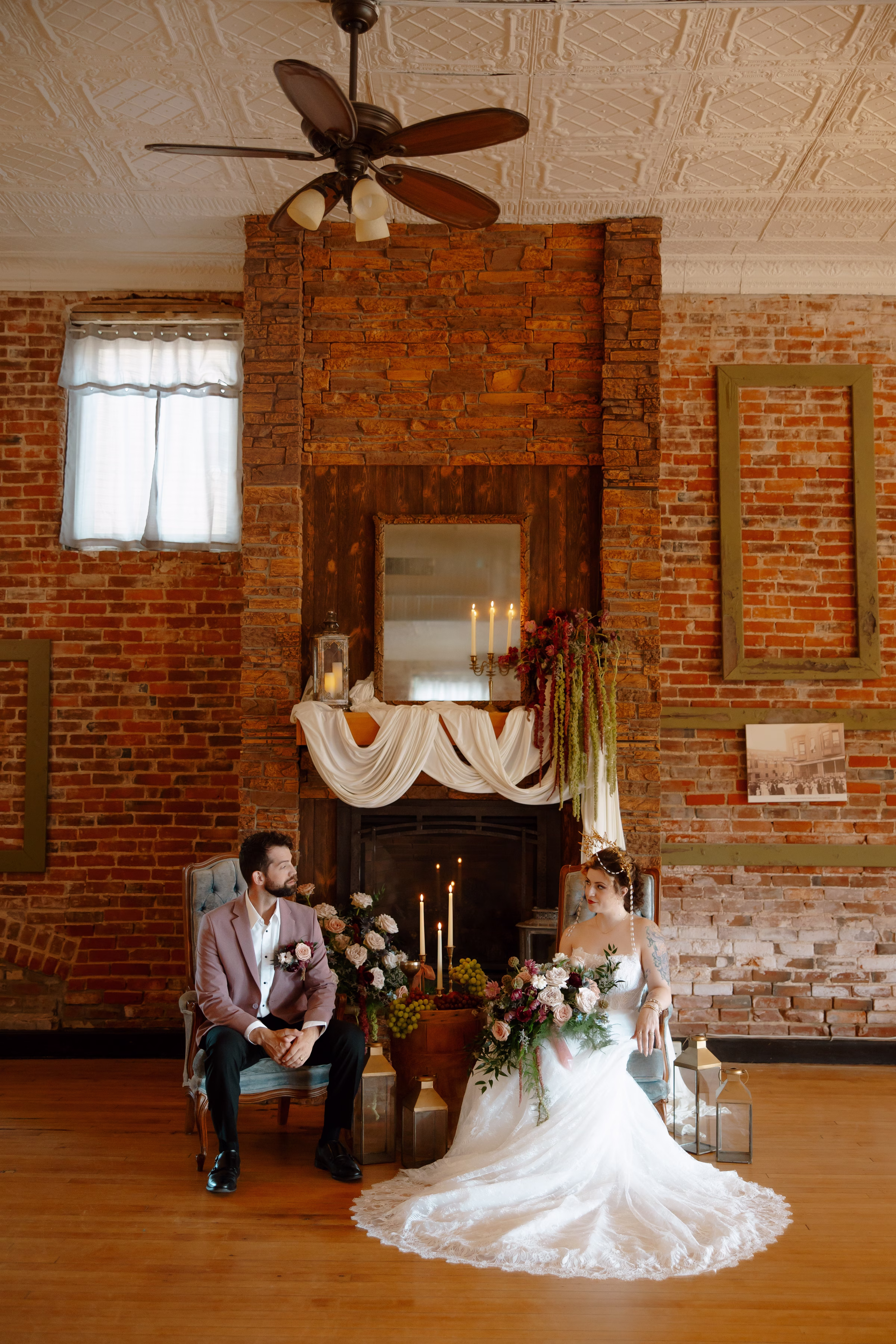 a full view of the wedding lounge, with the bride and groom both seated in dusty blue velvet chairs in front of the fireplace