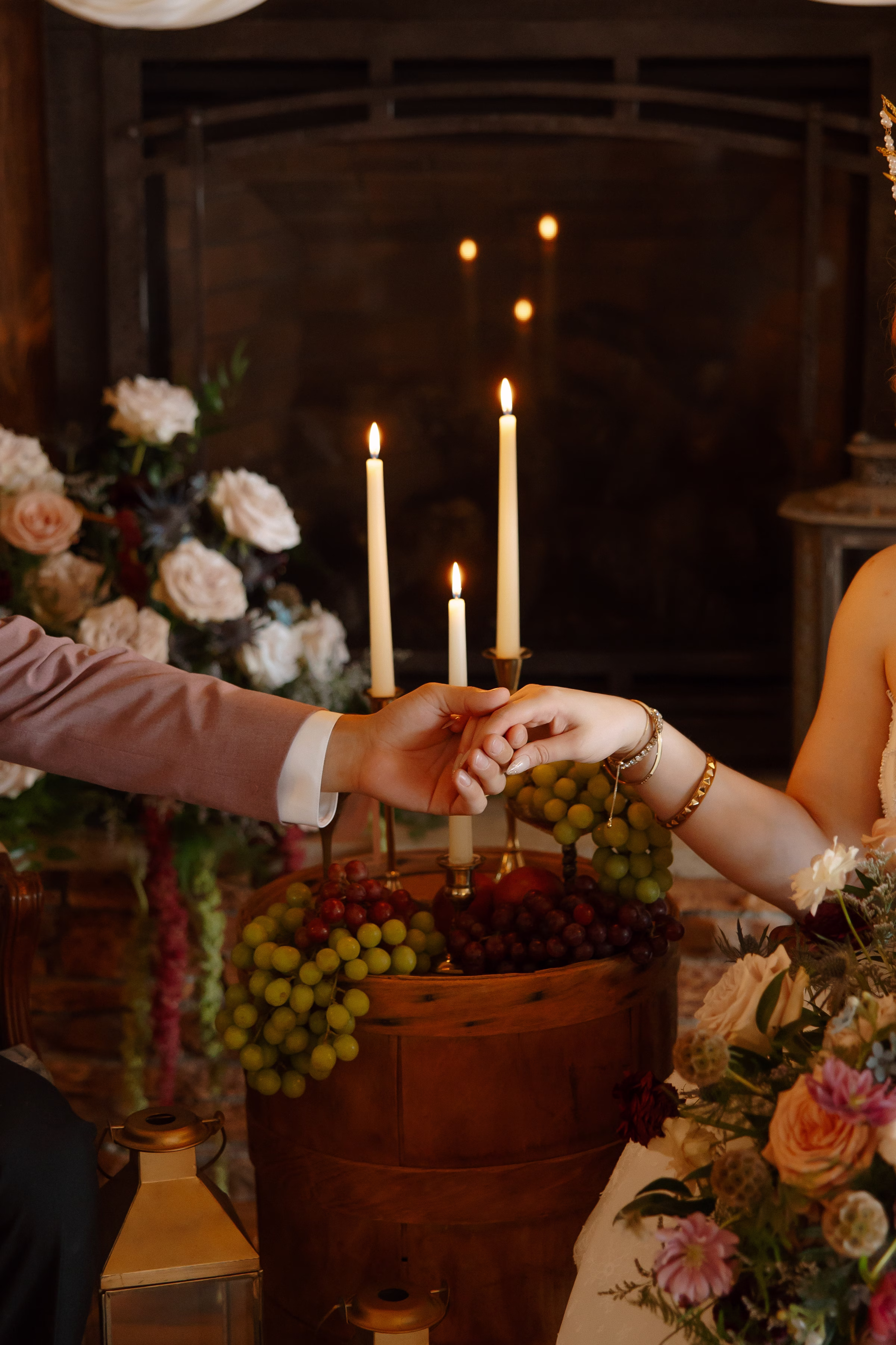 a detail photo of the couple holding hands in front of lit candles and fruit as décor int he lounge of the Midsummer Dream wedding styled shoot at B's Place Event Venue in West Salem, Wisconsin