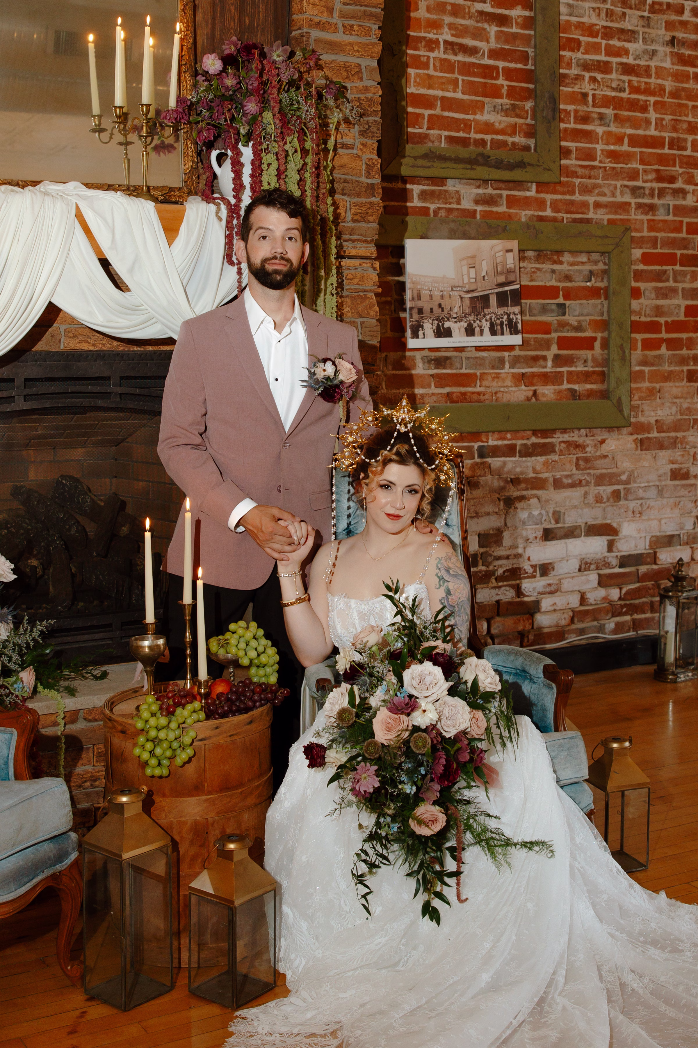 the bride and groom pose in the lounge, with the bride seated in a dusty blue velvet chair from Resource Vintage Rental and the groom standing behind her