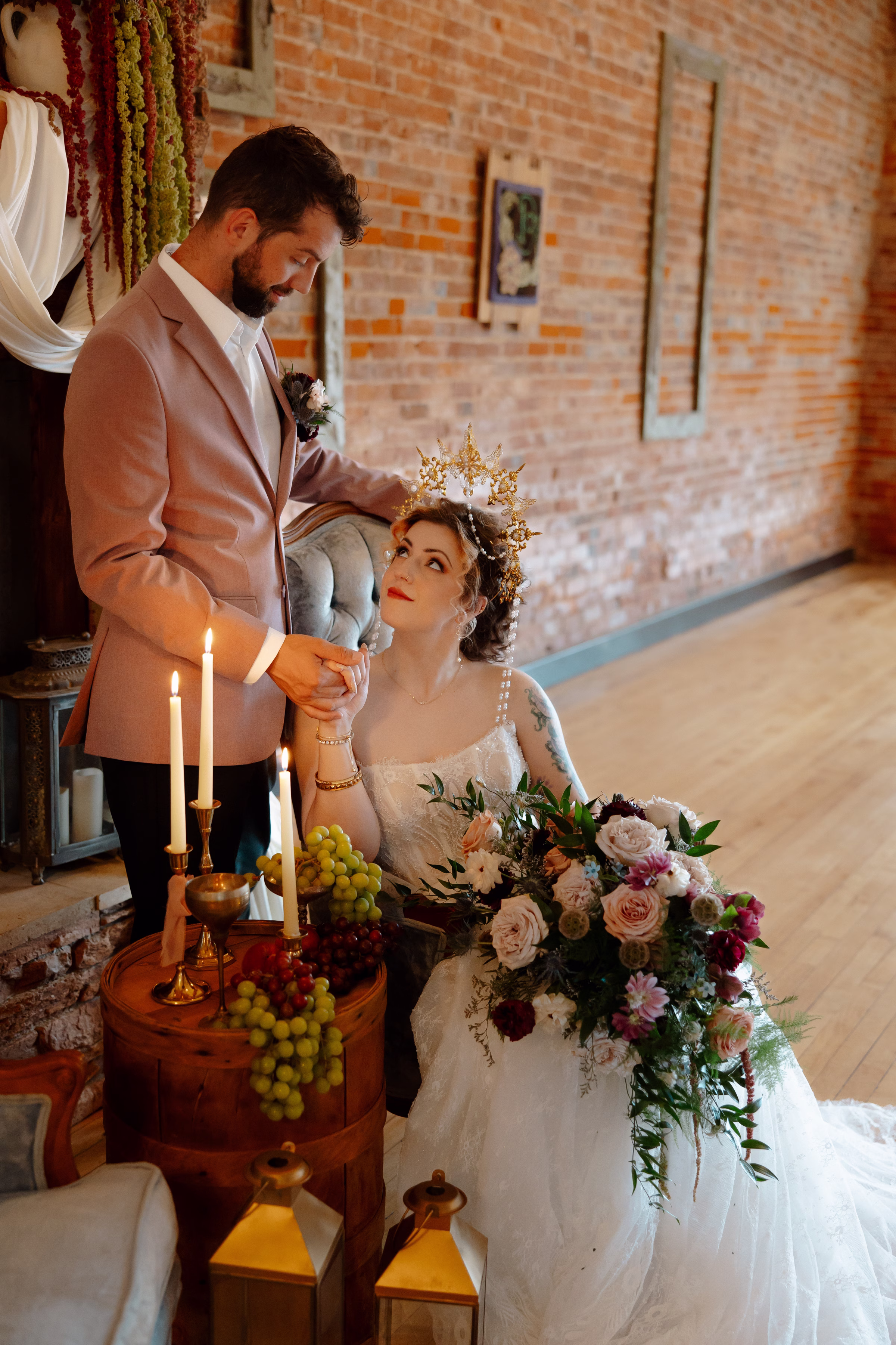 the bride and groom pose in the lounge, warmly lit by candlelight and holding hands. The bride holds her bridal bouquet on her lap