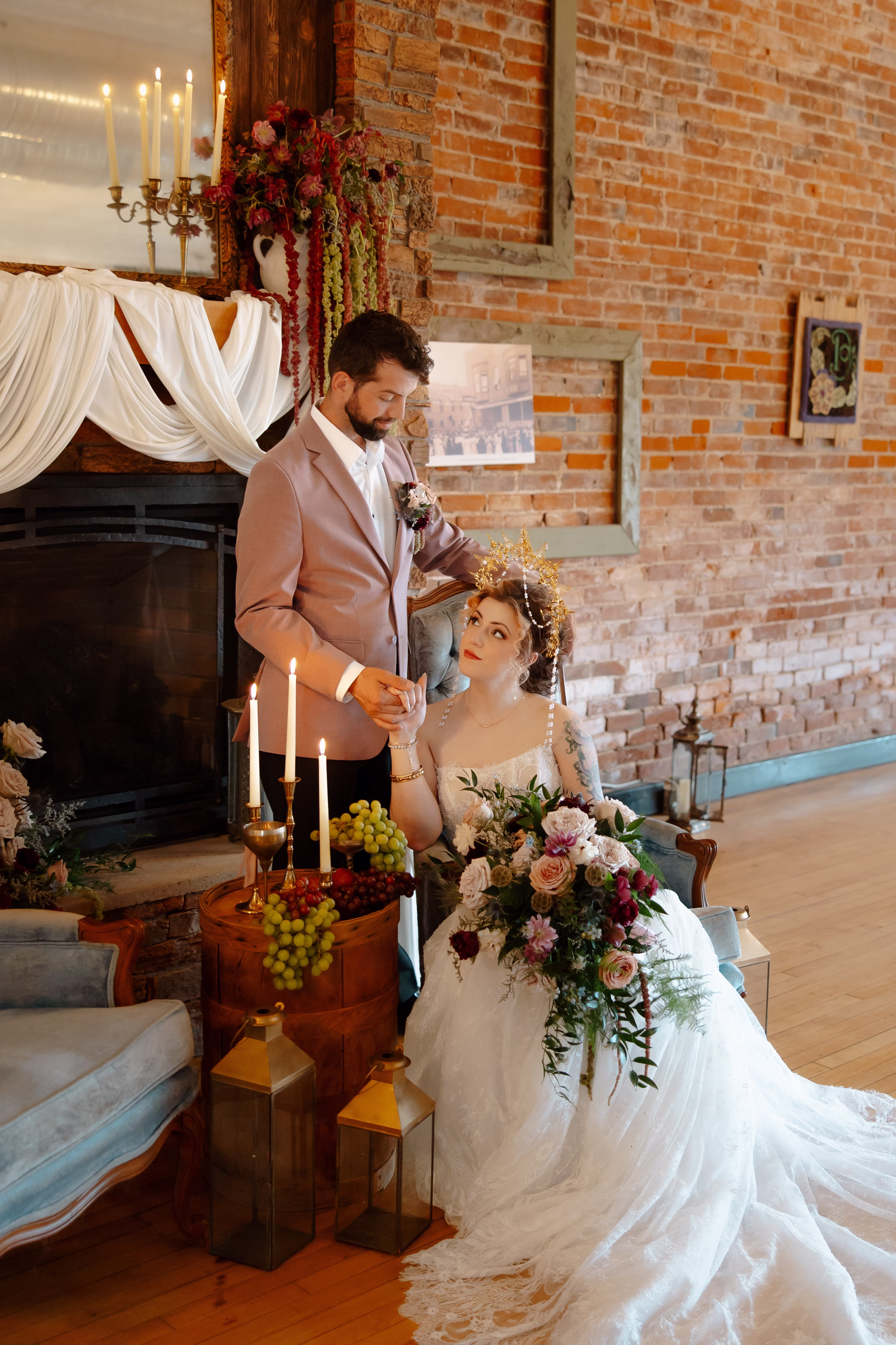 the bride and groom pose in the lounge at B's Place Event Venue in West Salem, Wisconsin, set against natural brick walls and a fireplace. The bride is seated and the groom is standing beside her