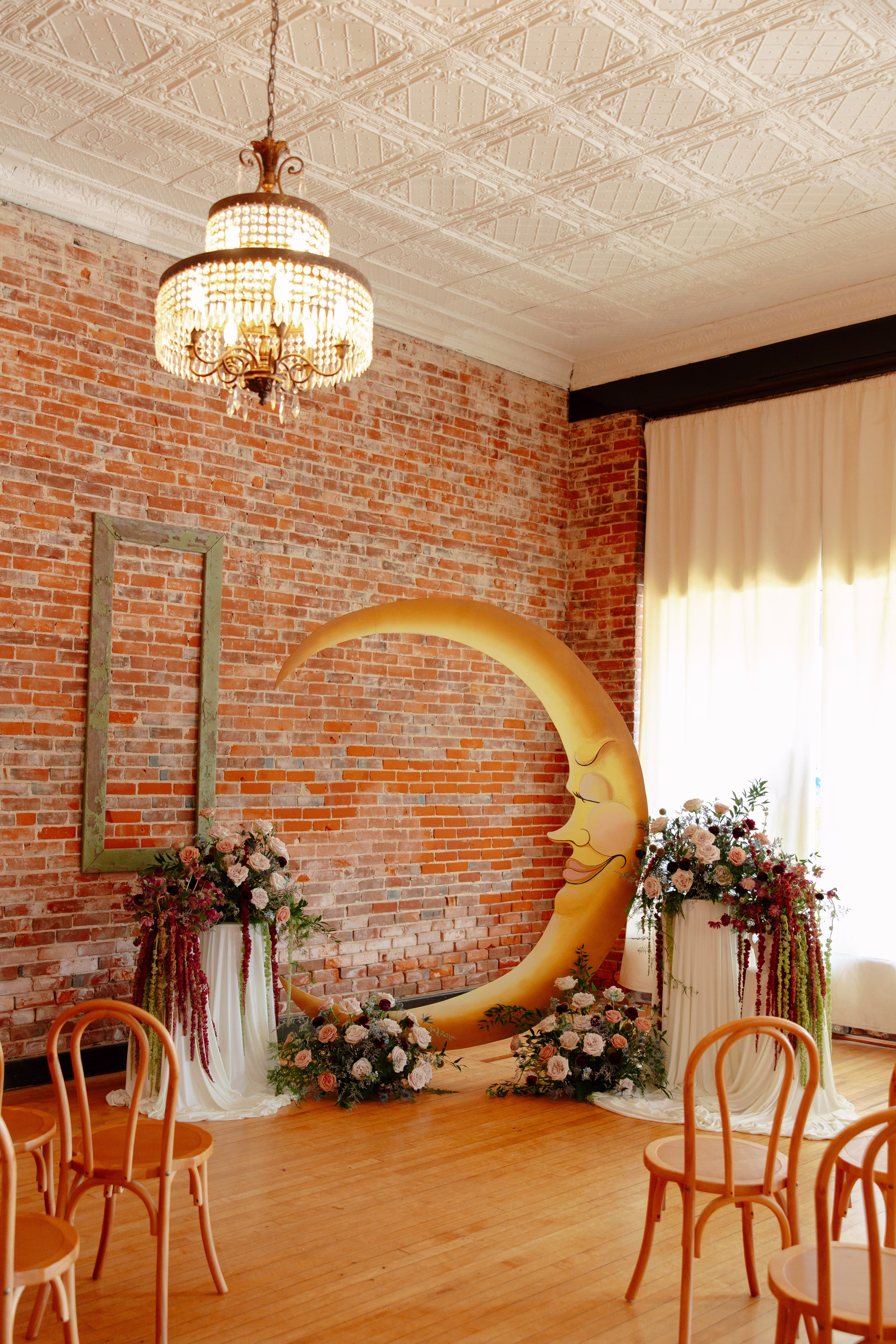 a view down the aisle of the wedding ceremony backdrop featuring serene painted moon surrounded from ground florals and florals on pedestals