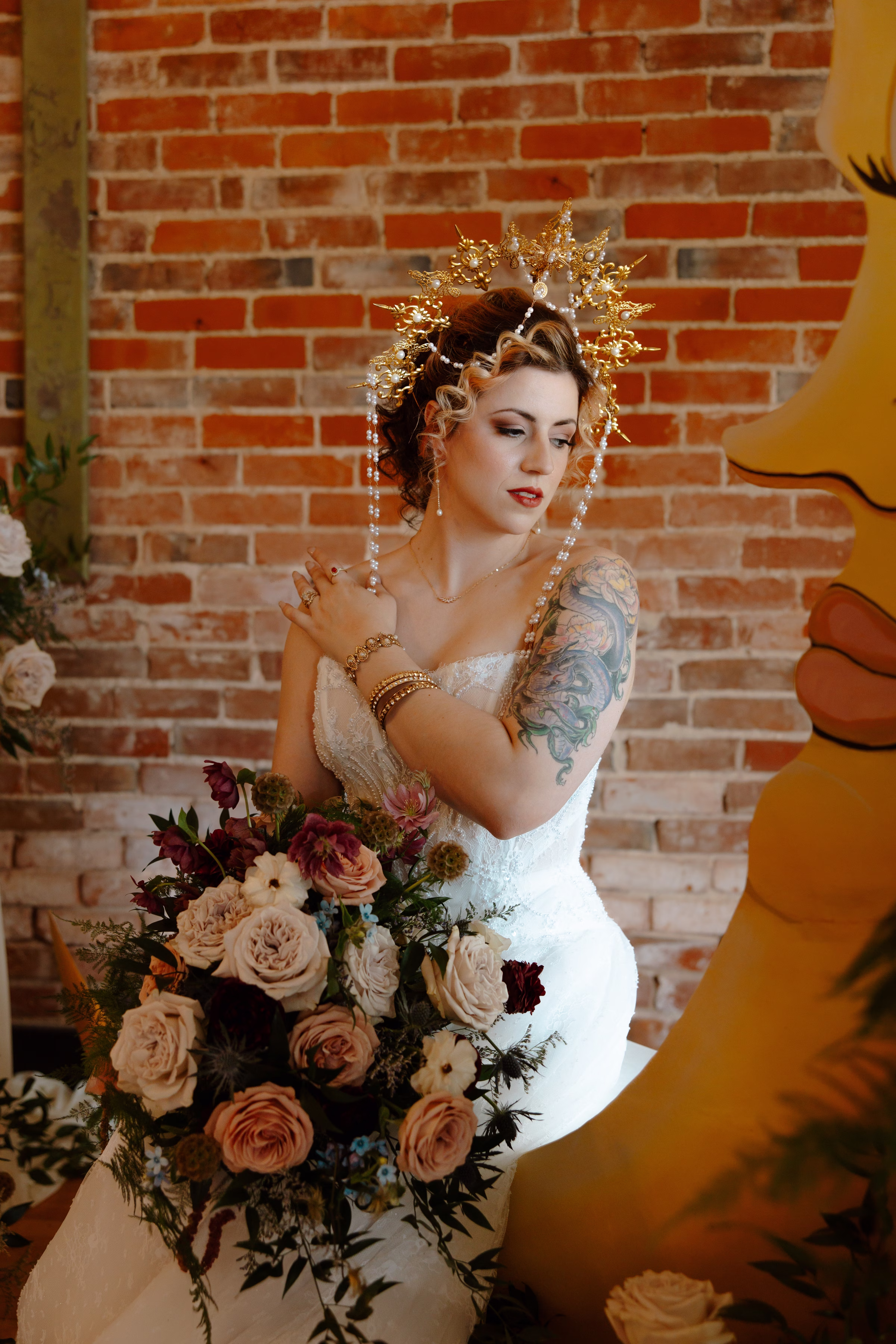 bride poses by the ceremony backdrop wearing ornate golden crown and an oversized bridal bouquet from Bloom & Knot