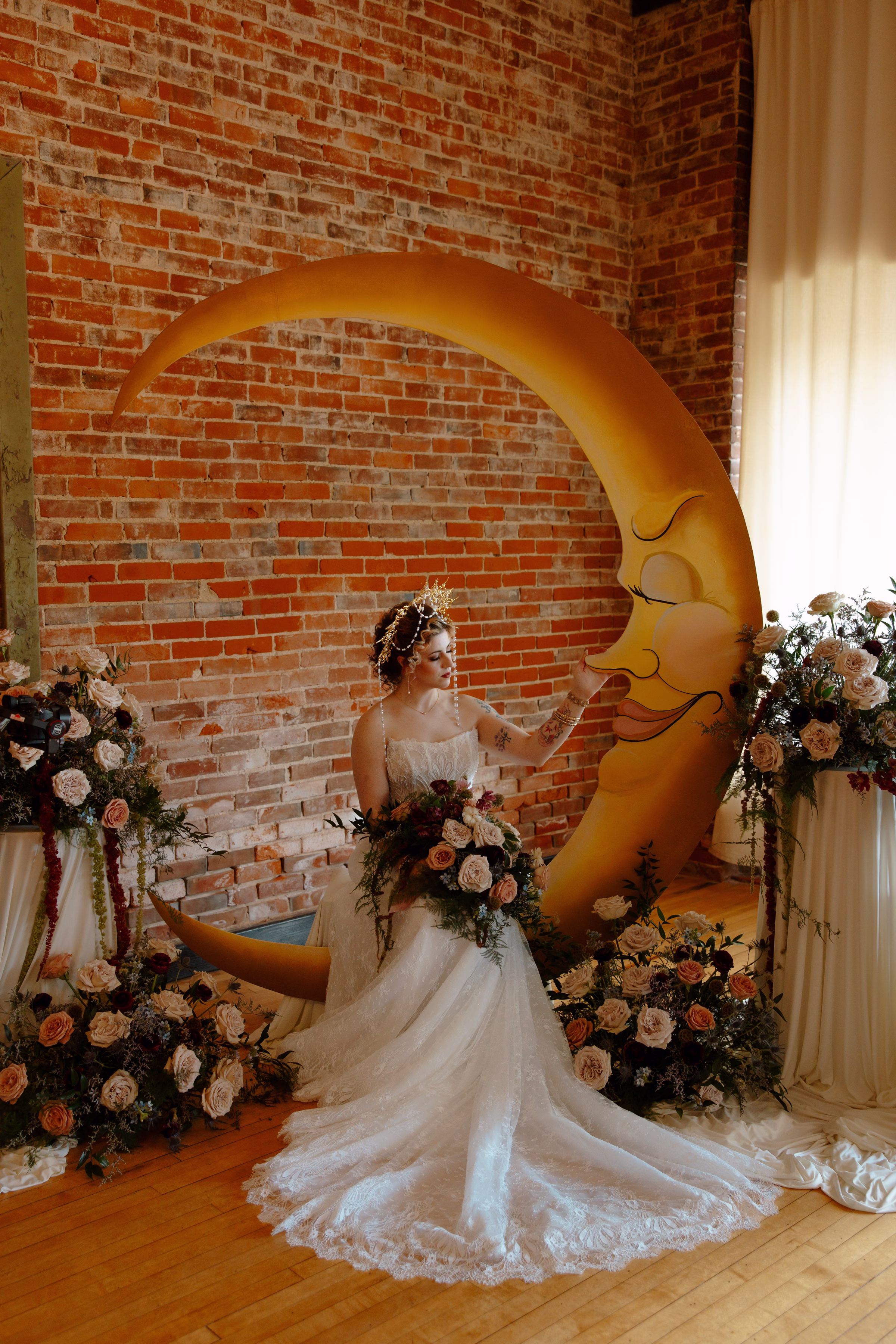 the bride is seated at the ceremony setup, placing a hand on the serene painted moon backdrop