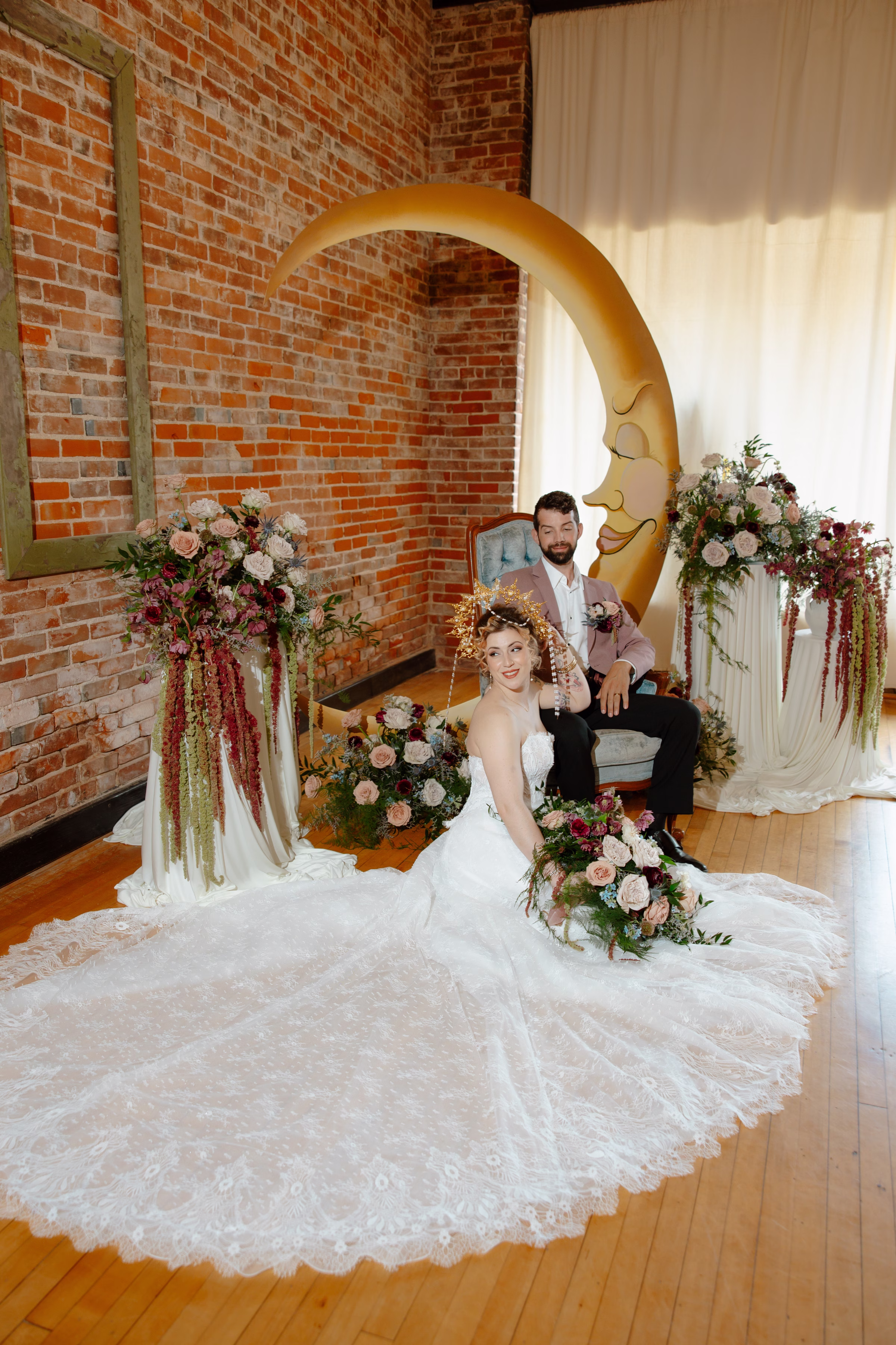 the couple lounges at the ceremony backdrop, with the groom seated and the bride sitting on the floor, showcasing the long train of her dress from Charlotte's Bridal & Formal Wear