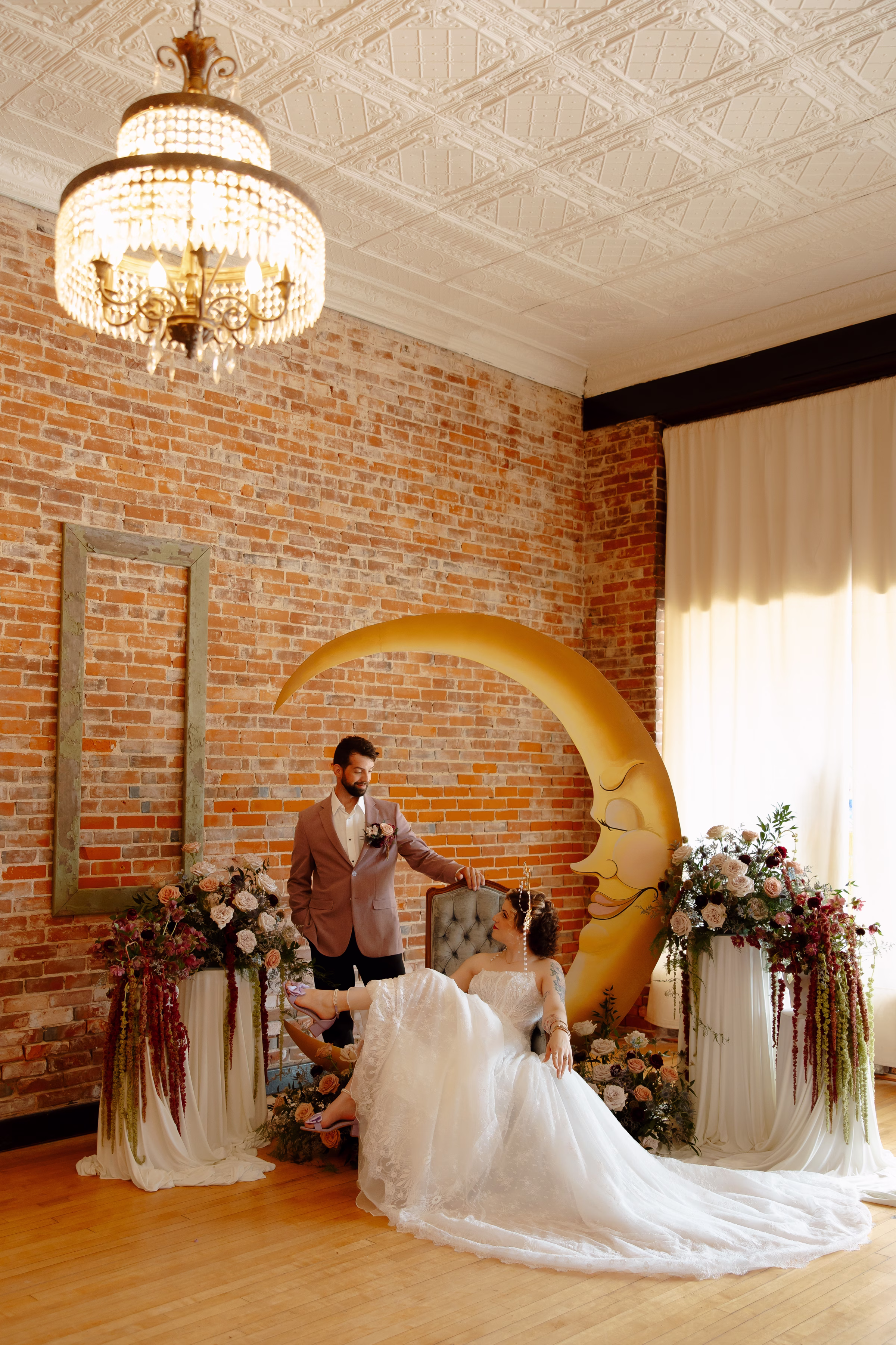 the bride and groom models lounge by the ceremony backdrop, with the bride seated, feet kicked up, and the groom standing behind her