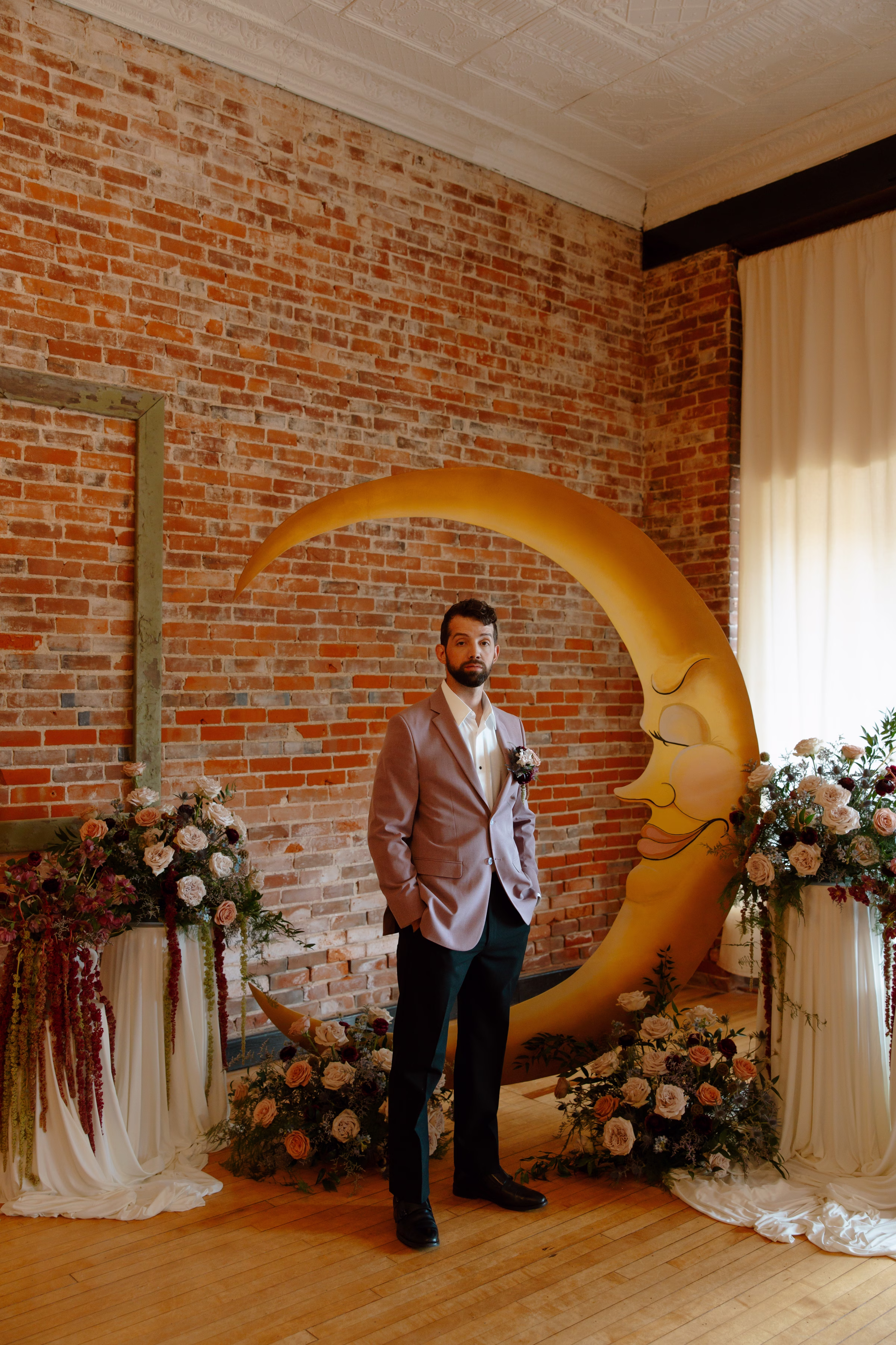 the groom stands in front of the crescent moon celestial-inspired ceremony at B's Place Event Venue in West Salem, Wisconsin