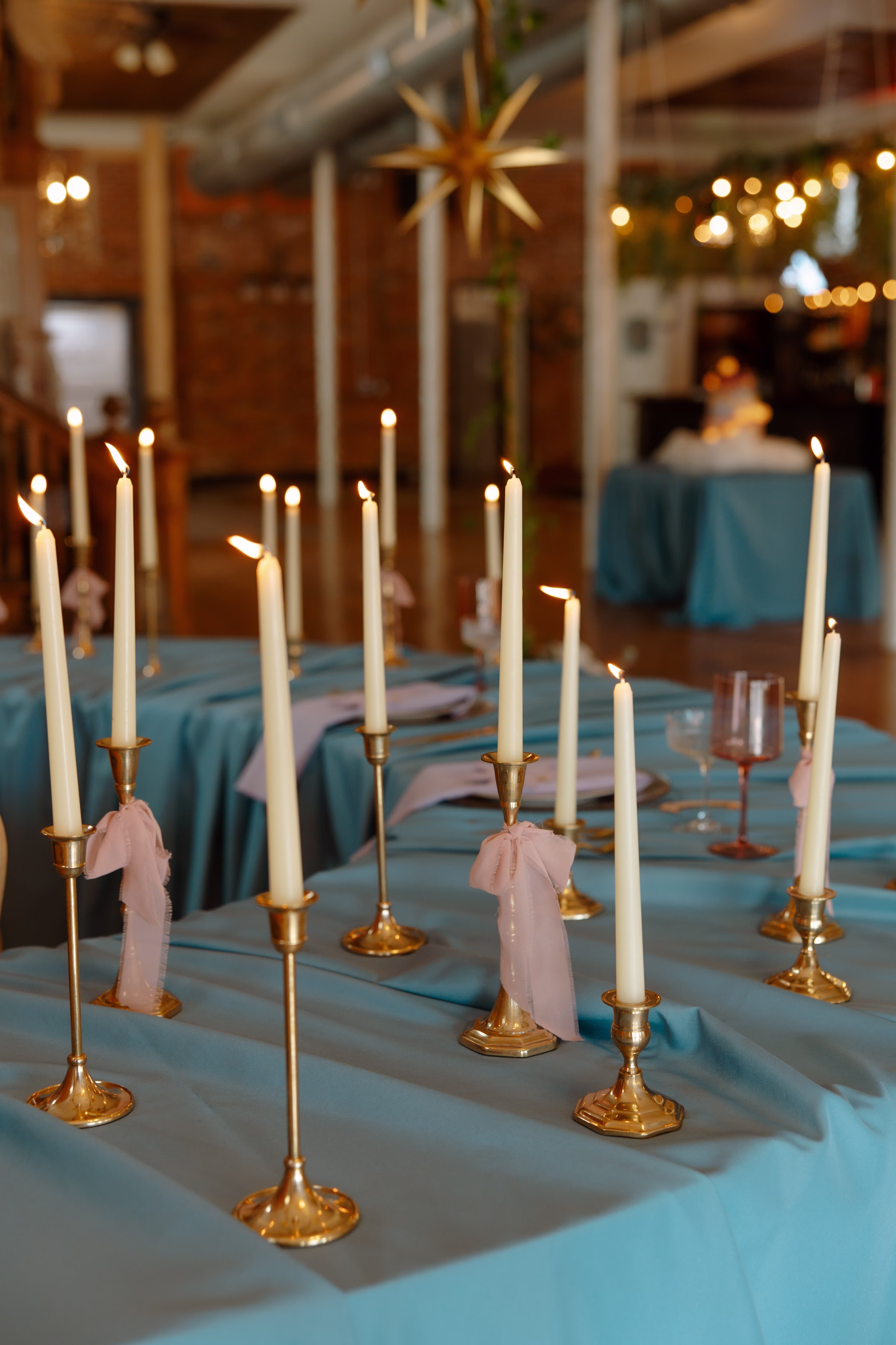 a detail photo showing lit candles on gold candlesticks of varying heights. A few of the candlesticks are tied with blush ribbons