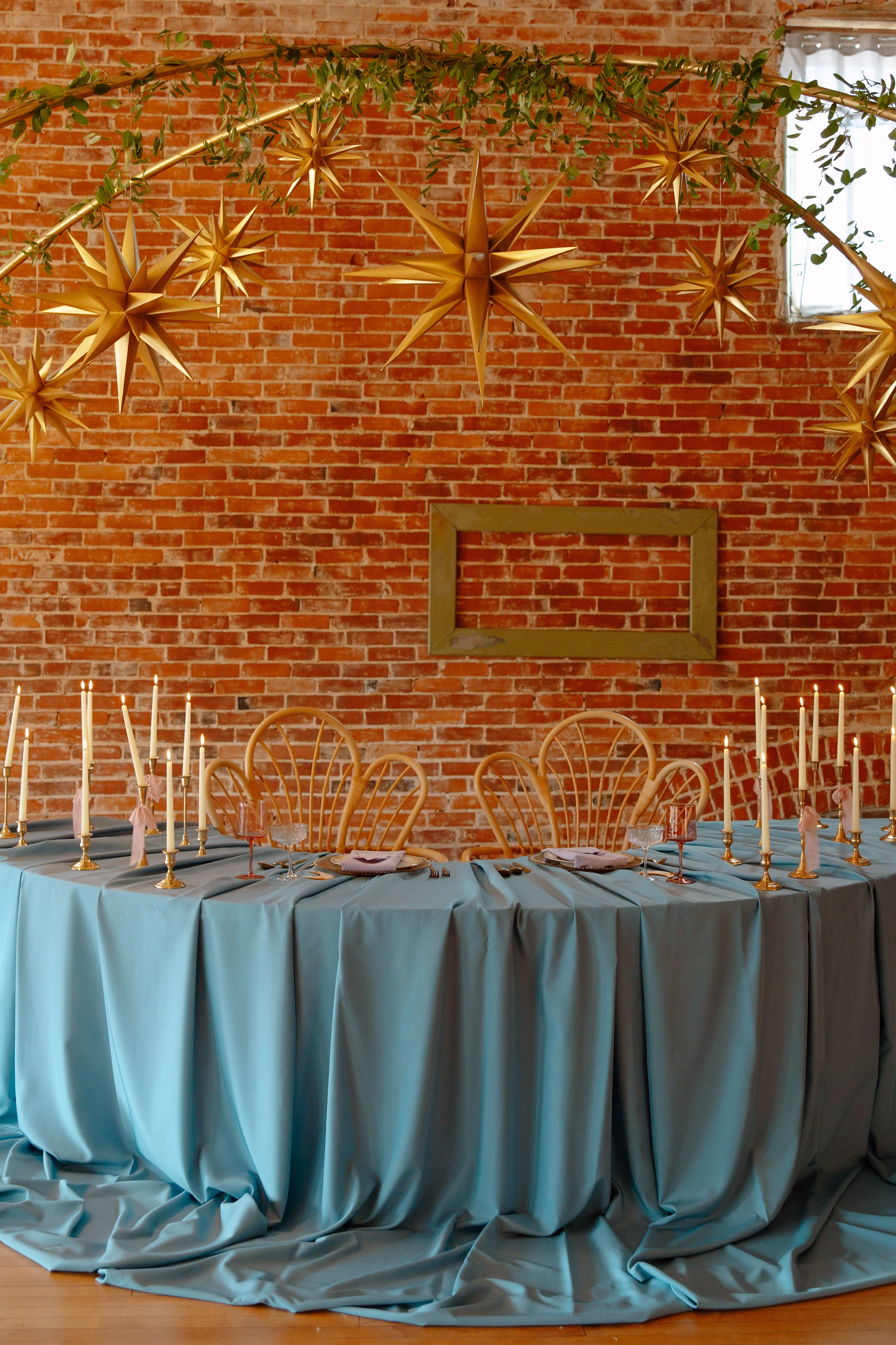 a front-view of the sweetheart table, with blue tablecloth, lit candles, and hanging stars overhead