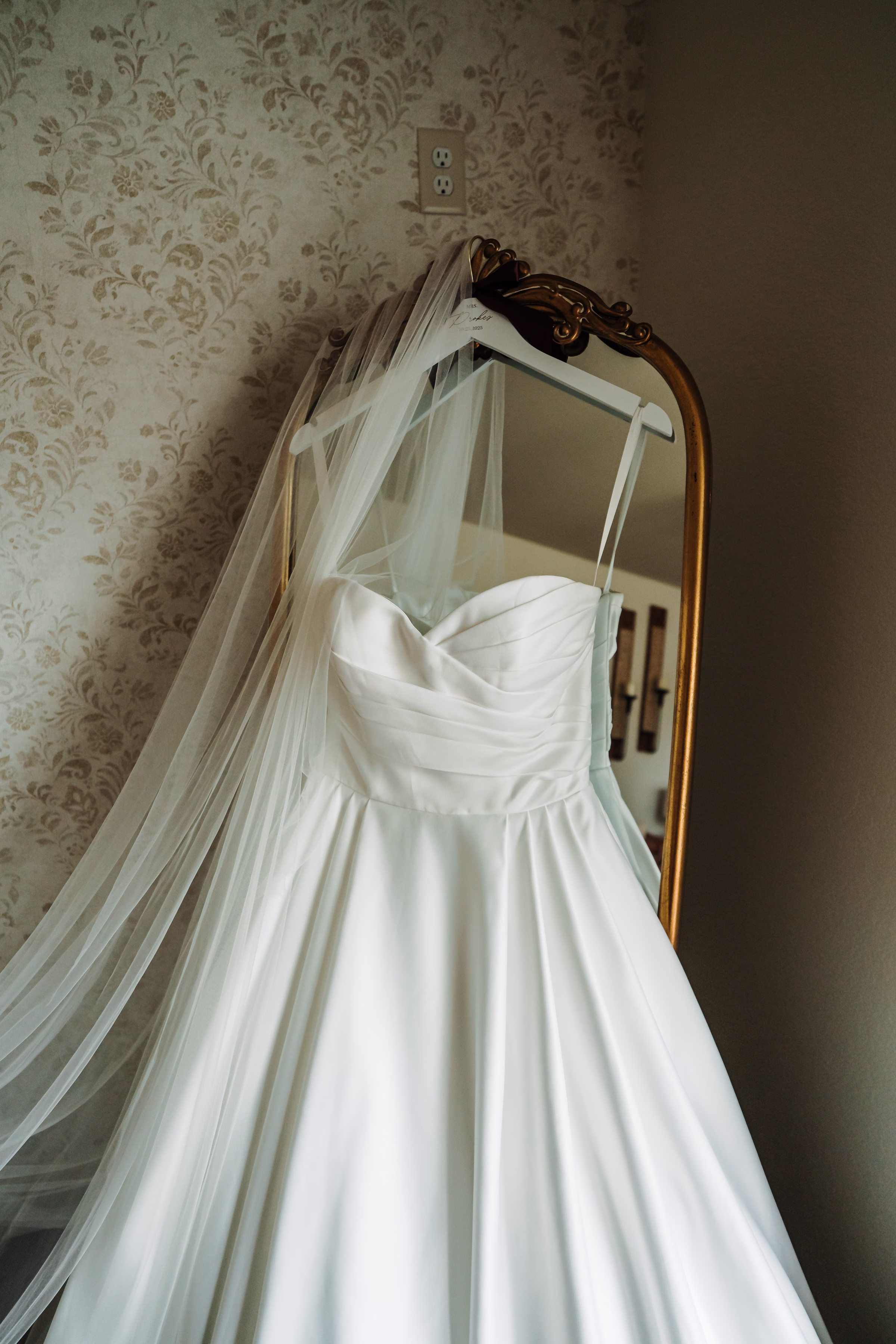 scenic fall wedding winnebago springs minnesota bridal preparation 3579 - An Elegant Fall Wedding at Winnebago Springs | Emma & Tyler a bridal gown from Charlotte's Bridal & Formal Wear hangs from a vintage mirror. The understated, A-line dress has a sweetheart neckline, a pleated bodice and a full skirt