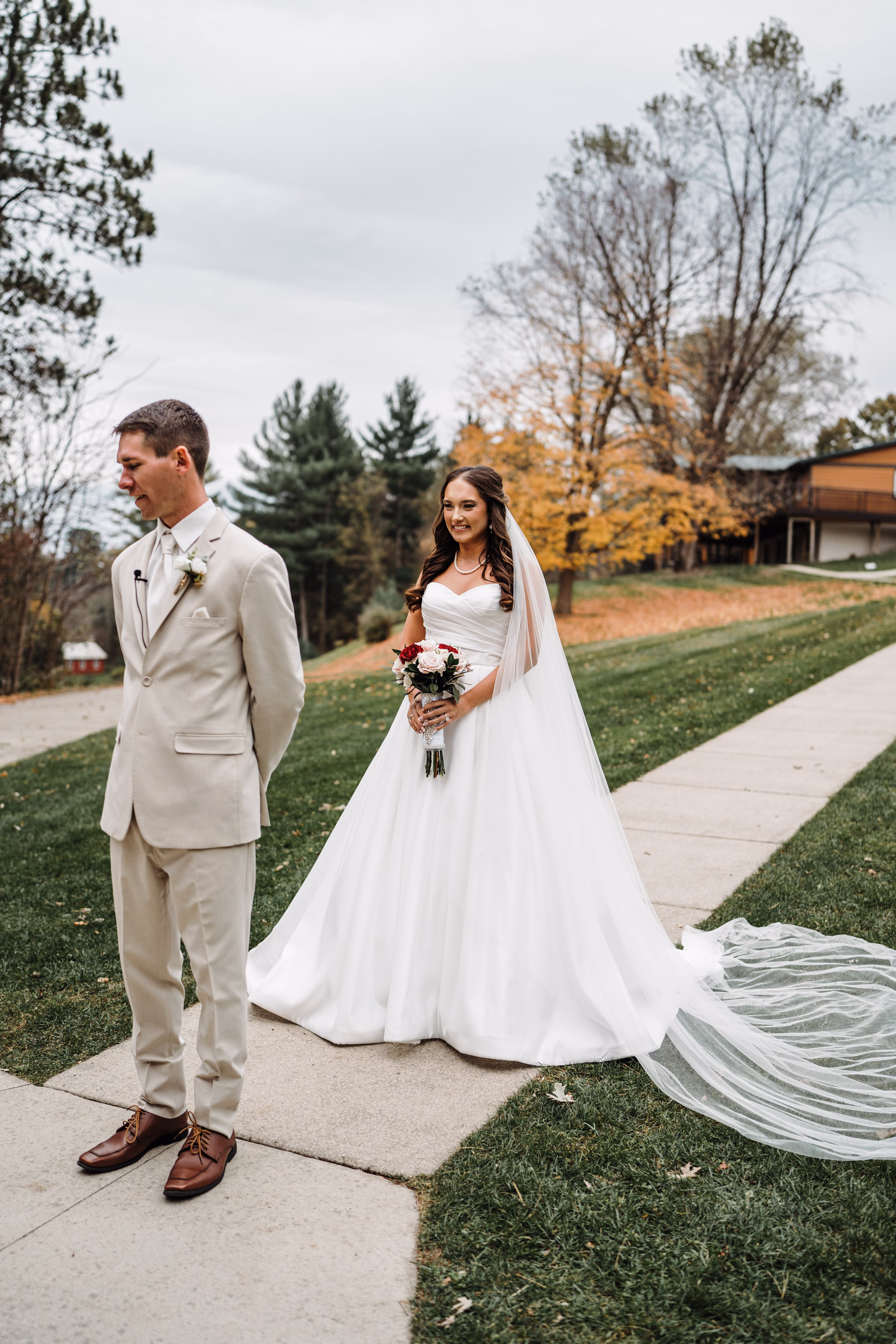 scenic fall wedding winnebago springs minnesota first look 3822 - An Elegant Fall Wedding at Winnebago Springs | Emma & Tyler a bride and groom stand outside, preparing for a first look. The bride is standing behind the groom, holding her bouquet, and waiting for him to turn around