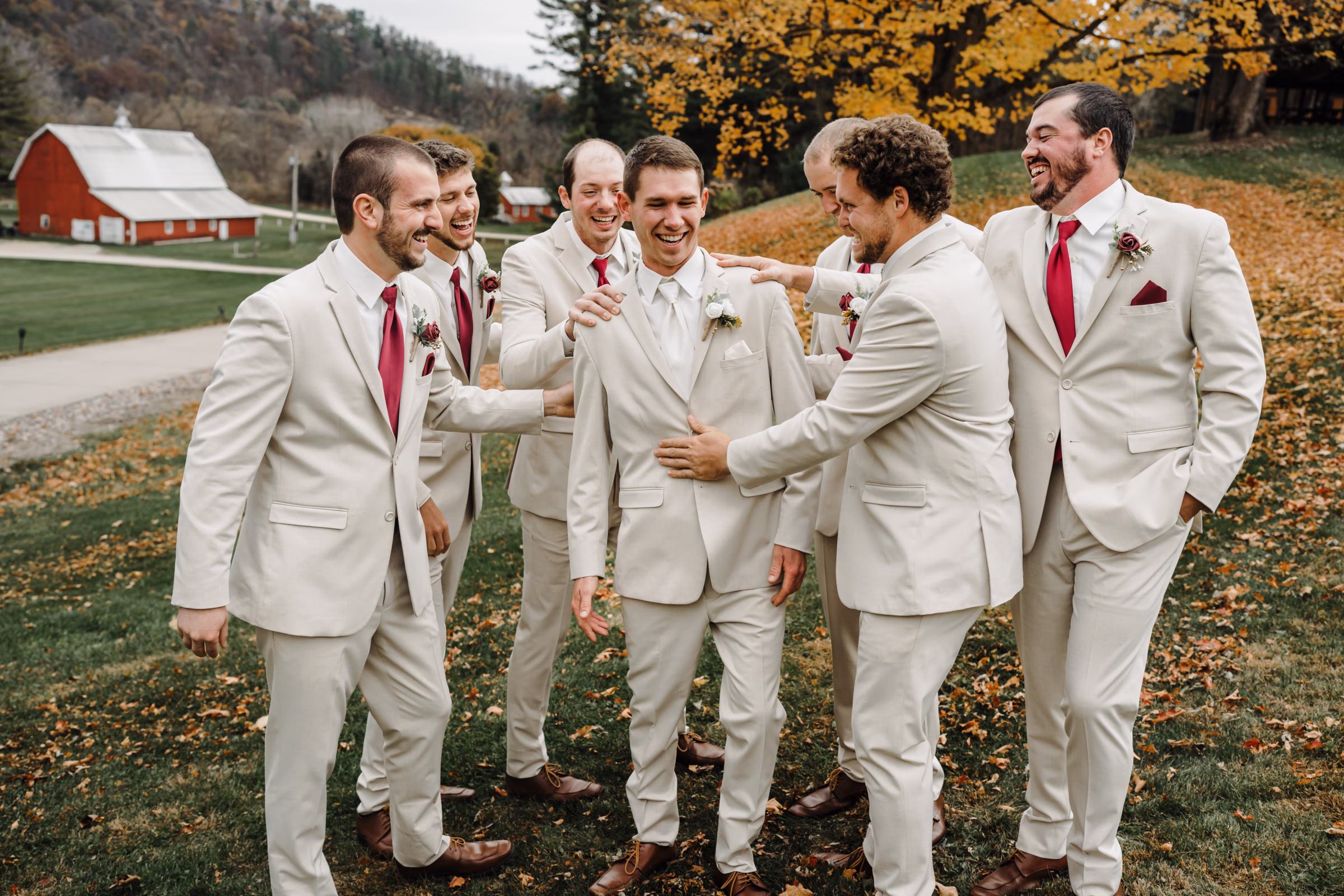 scenic fall wedding winnebago springs minnesota groomsmen 0838 - An Elegant Fall Wedding at Winnebago Springs | Emma & Tyler a groom is surrounded by his groomsmen, smiling and preparing to celebrate. bold orange fall-colored leaves are on the ground behind them