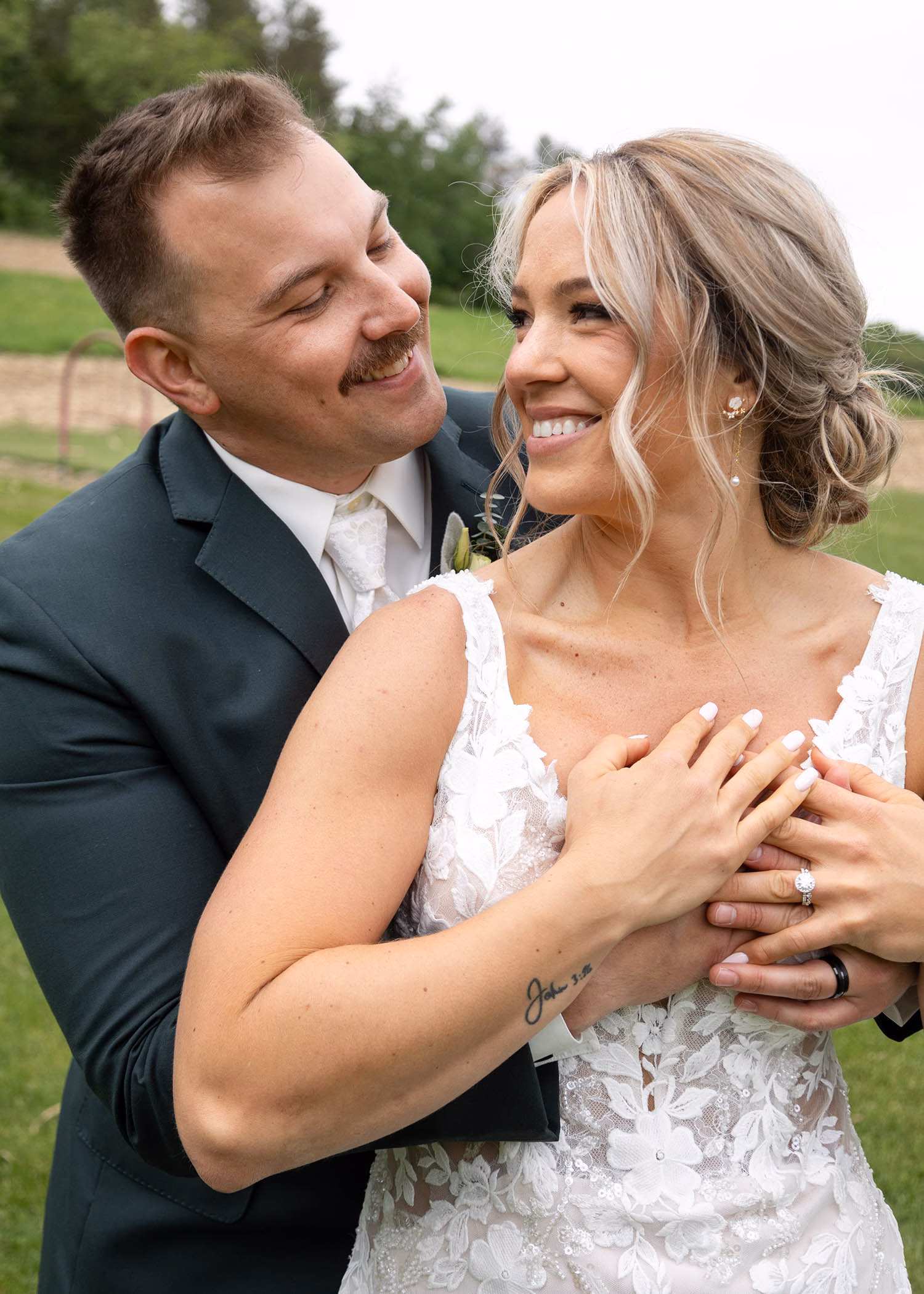 A groom embracing his smiling bride from behind while holding hands to display her diamond engagement ring, captured by La Crosse, Wisconsin wedding photographer Captured by Nancy Christine Photography.