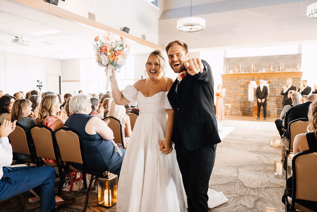 Joyful newlyweds walking down the aisle during an indoor wedding ceremony at La Crescent Area Event Center.