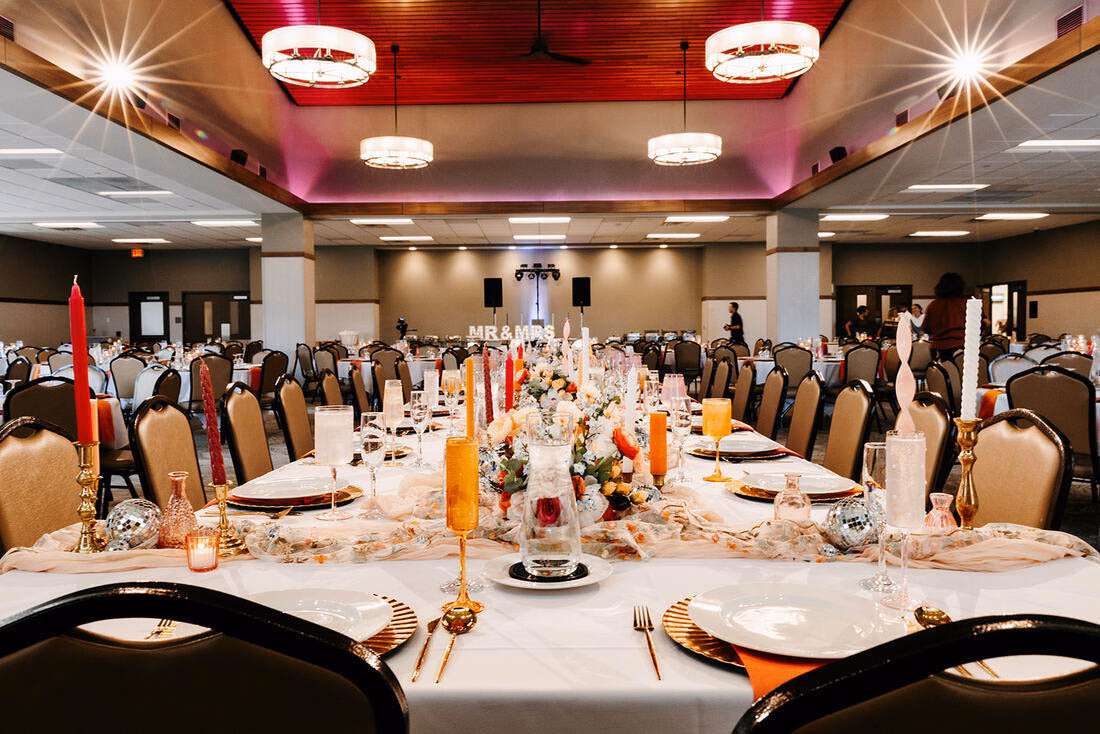 Vibrant wedding head table at La Crescent Area Event Center with colorful taper candles, floral runners, and a glowing "MR & MRS" sign in the background.
